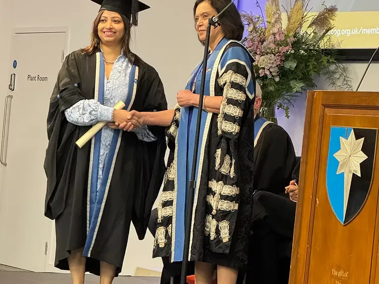 Dr. Swati Shree in graduation robes receiving a certificate at a ceremony.